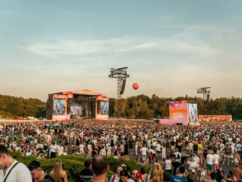 Tłum ludzi na festiwalu bittersweet, dwie sceny, ekrany z grafikami i pomarańczowy balon na niebie.
