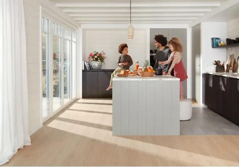 Une famille prépare un repas dans une cuisine moderne. La **délimitation sol cuisine salon** est subtile, avec un parquet clair contrastant avec le carrelage du salon.
