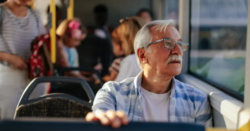 Starszy pan w okularach, podróżujący autobusem w Szczecinie, zastanawia się, czy 70 latek płaci za komunikację miejską.