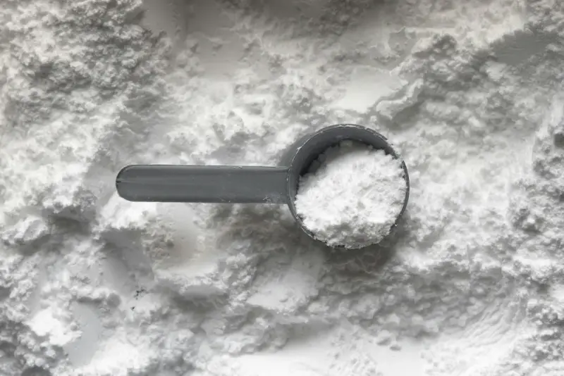 Miarka z białym proszkiem, prawdopodobnie disodium edta, na tle sypkiego materiału.
