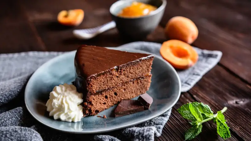 Ein Stück Sachertorte, das aussieht wie vom Original Sachertorte Rezept, mit Schlagobers, Schokolade und Marillenmarmelade.