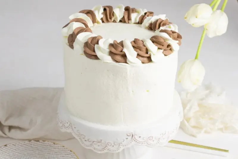 Tarta blanca con borde de nata y chocolate, lista para celebrar.