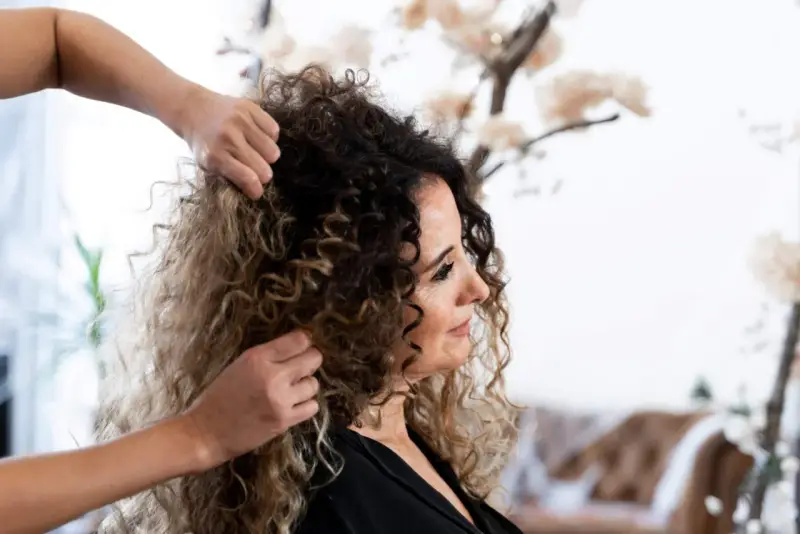 Stylista układa kręcone włosy klientki, przygotowując się do strzyżenia. Wskazówki, jak obciąć kręcone włosy, pomogą uzyskać idealny kształt.