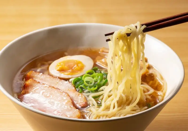 Parujące miseczka ramenu z makaronem, plastrami mięsa, jajkiem i szczypiorkiem. Idealne ramen przyprawy podkreślają smak.