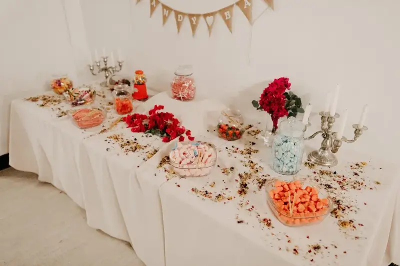Elegante candy bar boda con dulces de colores, flores rojas y candelabros plateados.