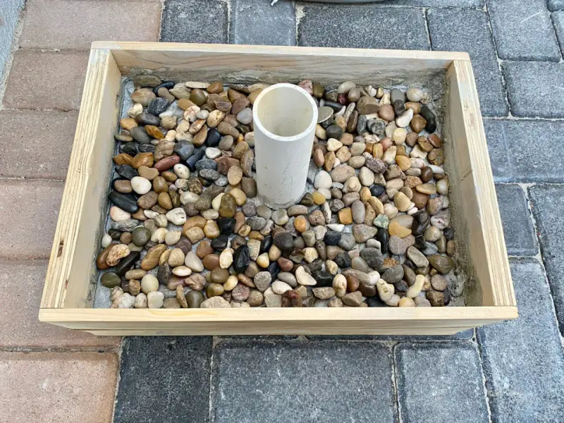 Base per ombrellone fai da te: un contenitore in legno riempito di ghiaia con un tubo centrale per l'asta.