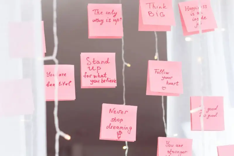 Rosa Haftnotizen mit inspirierenden Affirmationen wie "Think BIG" und "Never stop dreaming" hängen an einer Lichterkette.