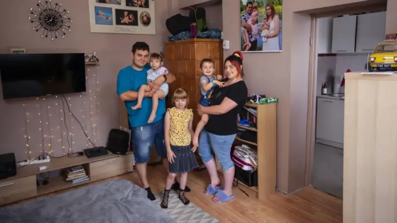 Rodzina z trójką dzieci pozuje do zdjęcia w salonie. W tle widać zdjęcia, telewizor i ozdobne lampki. Ich życie na kredyt nie przeszkadza im w cieszeniu się chwilą.