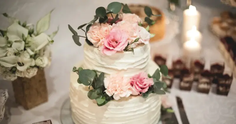 Elegancki tort weselny z kremową dekoracją i pastelowymi kwiatami, ozdobiony gałązkami eukaliptusa.