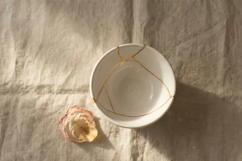 Biała miska z pęknięciami zespolonymi złotem, jak w kintsugi, obok zasuszonego płatka róży. Symbolizuje proces leczenia, jak w przypadku osobowości borderline test.