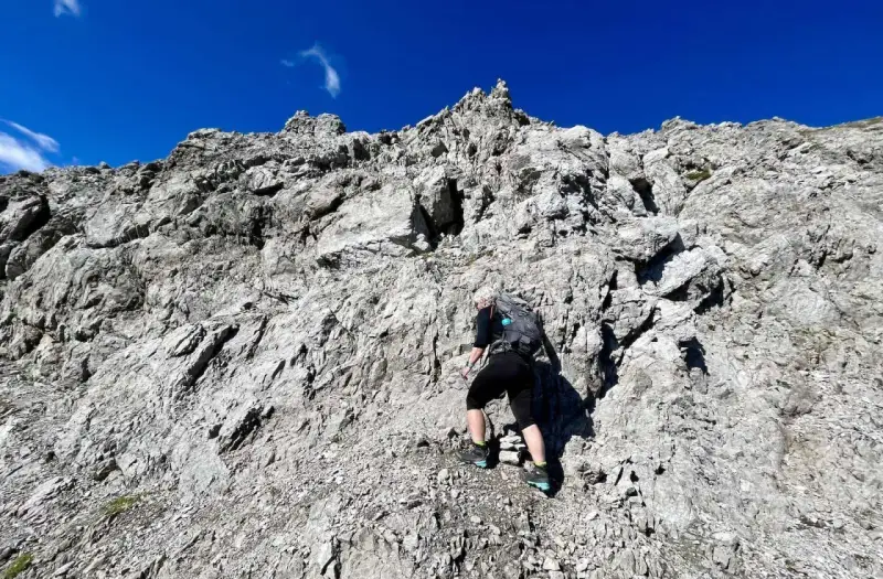 Bergsteigerin klettert über felsiges Gelände, das der UIAA-Skala entspricht. Blauer Himmel und schroffe Felsen.