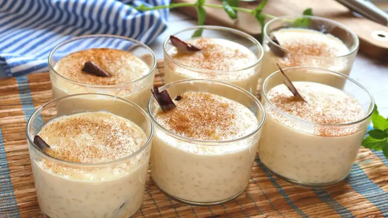 Seis vasitos de cremoso arroz con leche, espolvoreados con canela y decorados con una ramita de canela.