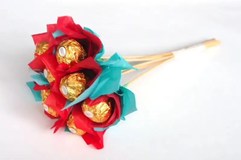 Un ramo de bombones dorados envueltos en papel rojo y turquesa, ideal para un regalo dulce y original.