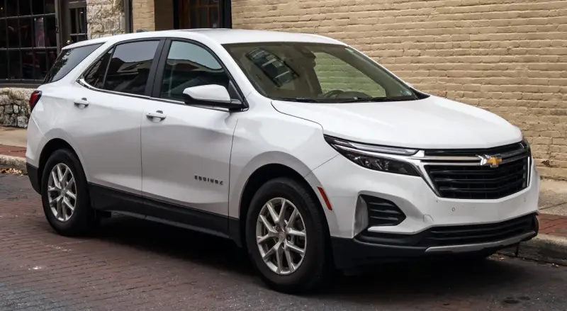 Biały Chevrolet Equinox stoi zaparkowany na brukowanej ulicy, obok ceglanego budynku.