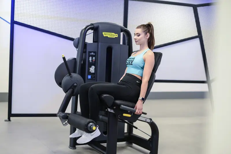 Kobieta wykonuje wyprosty nóg na maszynie Technogym, ćwicząc mięśnie czworogłowe uda.