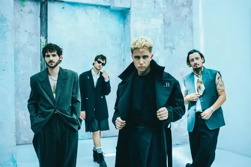 Le groupe Last Train pose devant un mur bleu clair, quatre hommes aux styles audacieux.