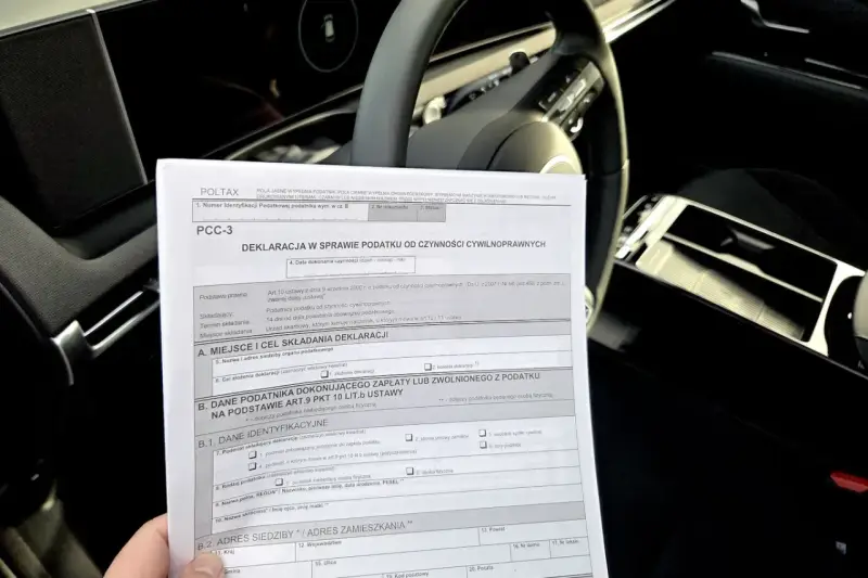 Deklaracja PCC-3, dokument dotyczący podatku od kupna samochodu, leży na desce rozdzielczej auta.