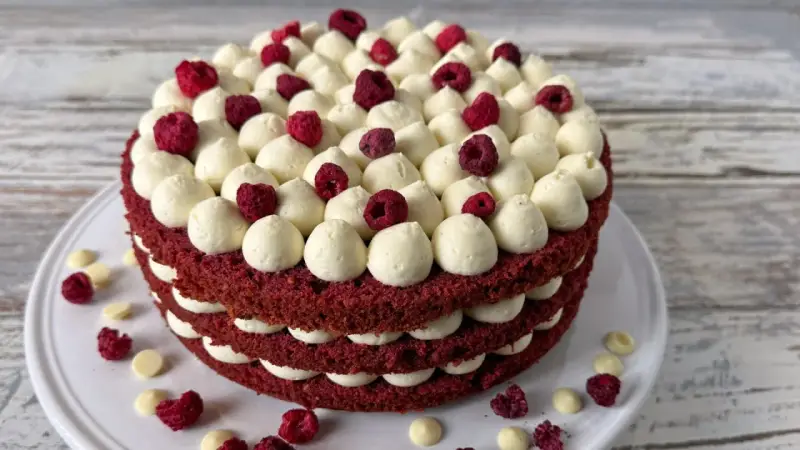 Ein mehrschichtiger Red Velvet Kuchen mit weißer Creme und Himbeeren.