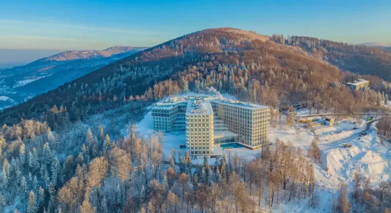 Nowoczesny hotel Crystal w zimowej scenerii, otoczony ośnieżonym lasem. To idealne miejsce na wypoczynek w Wiśle, górskim kurorcie.