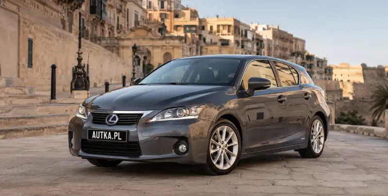 Szary Lexus CT 200h zaparkowany na brukowanej uliczce z zabytkowymi budynkami w tle.