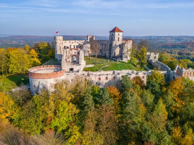 Ruiny zamku na wzgórzu, część szlaku Orlich Gniazd. Jesienne drzewa otaczają kamienne mury.