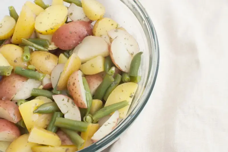 Insalata colorata di fagiolini e patate novelle, condita con erbe aromatiche, in una ciotola di vetro.