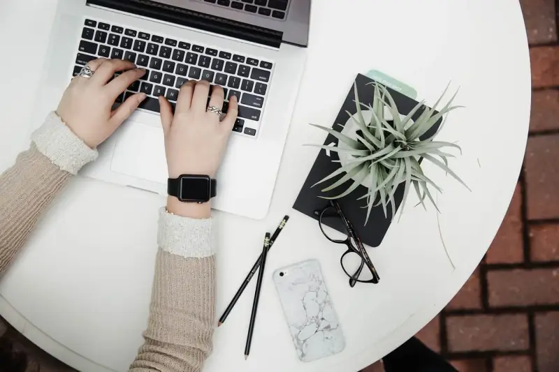 Kobieta pracuje na laptopie, obok leżą okulary, telefon i roślina. To idealne zdjęcia w chmurze do inspiracji.