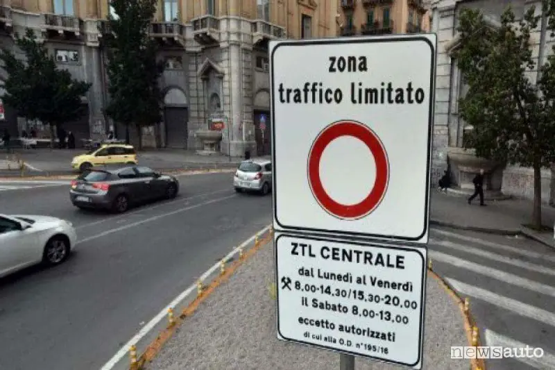 Cartello che indica "zona traffico limitato" con orari specifici. Auto in transito su strada urbana.