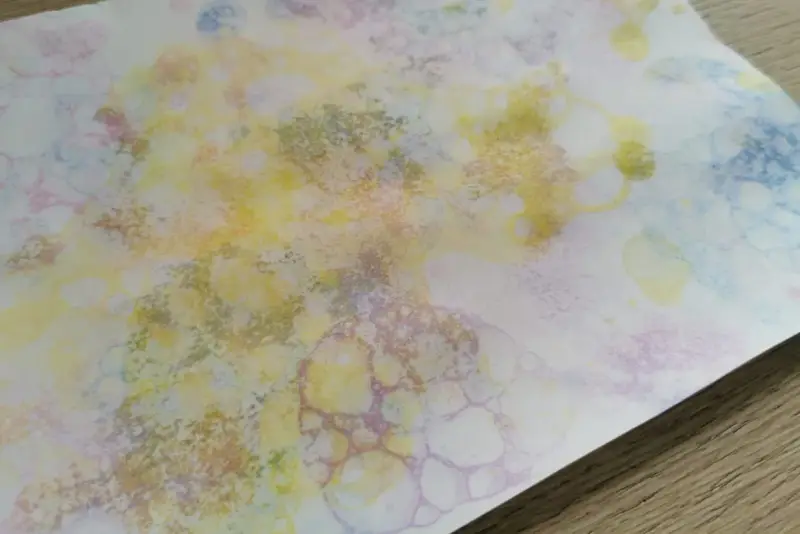 Peinture à bulles colorée sur papier blanc, avec des formes rondes et des éclaboussures.