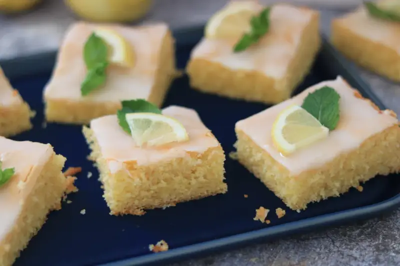 Saftige Kuchenstücke mit Zitronenguss, garniert mit Zitronenspalten und Minze. Ein Genuss, der nach dem besten zitronenkuchen der welt schmeckt.