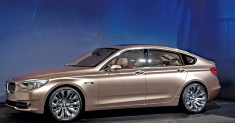 Eleganckie, złote bmw gt z przyciemnianymi szybami i chromowanymi felgami stoi na tle niebieskiej ściany.