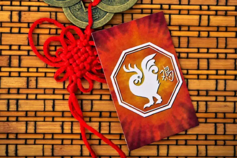 Czerwony sznur szczęścia i karta z białym kogutem, symbolem chińskiego zodiaku, na tle bambusowej maty.