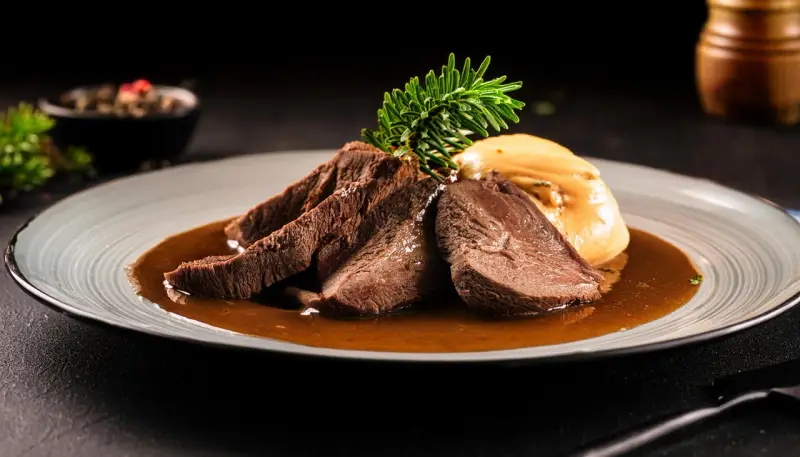 Zartes Tafelspitz-Rezept auf einem Teller mit Sauce, Beilage und Rosmarinzweig.