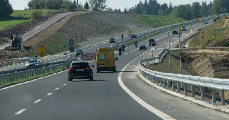Droga ekspresowa z samochodami i motocyklami, gdzie panuje bezpieczna prędkość. W tle widać prace budowlane.