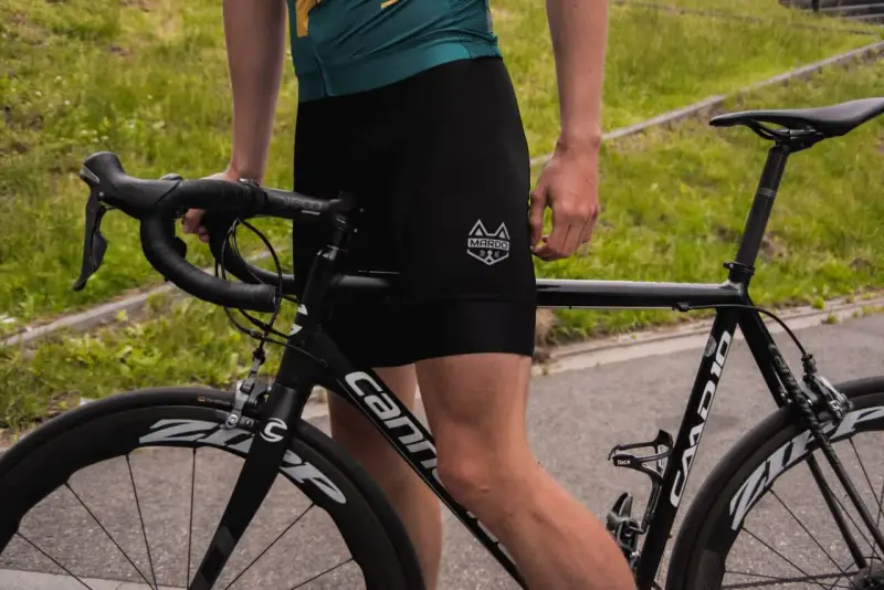 Kolarz w czarnych spodenkach i zielonej koszulce przygotowuje się do treningu kolarskiego. Rower szosowy Cannondale czeka na jazdę.