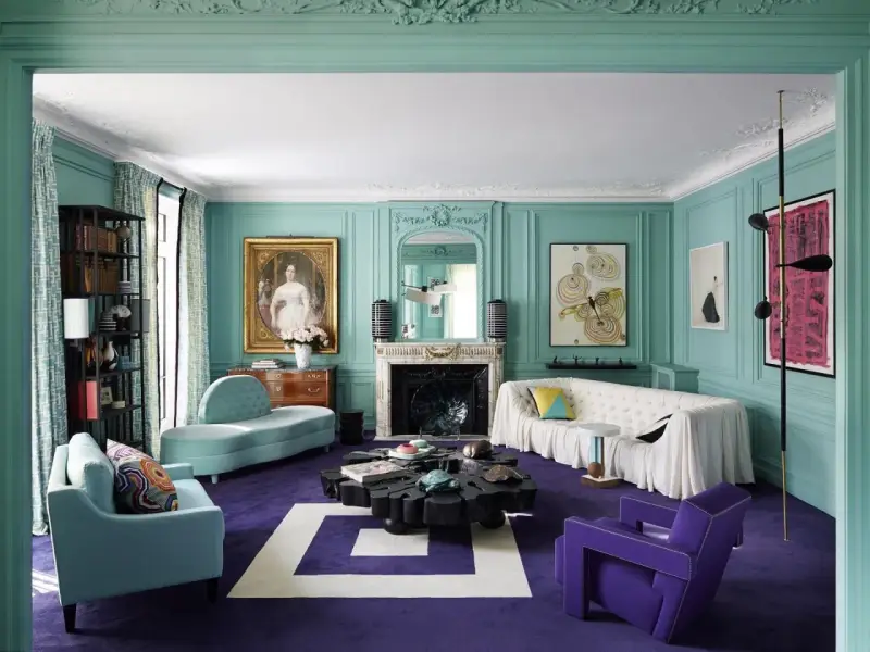 Sala de estar con paredes turquesas y alfombra morada. Muebles modernos y un retrato clásico crean un espacio amplio, ideal para aprender como pintar una habitacion para que se vea mas grande.