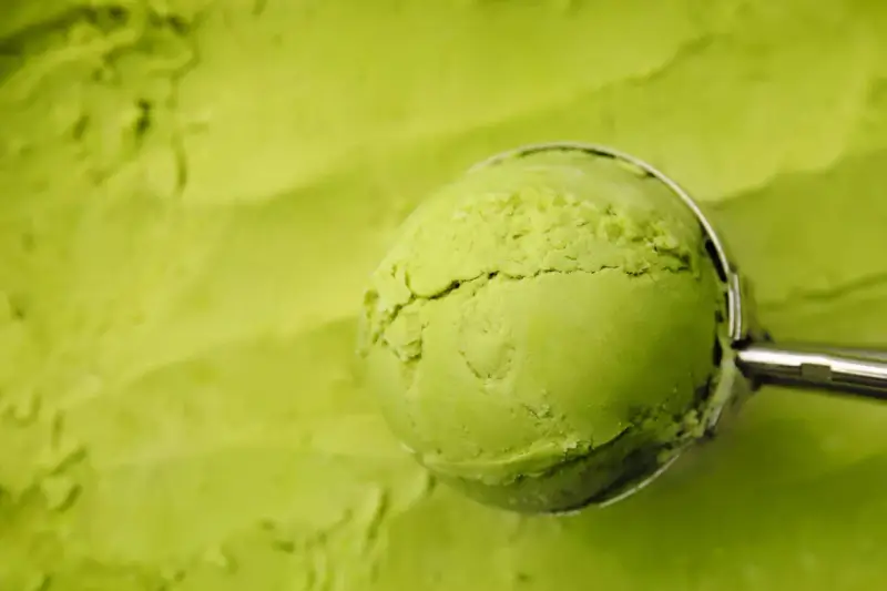 Eine Kugel cremiges Matcha-Eis wird mit einem Löffel aus einer Schüssel gehoben. Perfekt für ein erfrischendes Matcha Eis Rezept.