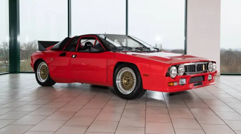 Czerwona Lancia 037 z czarnym spojlerem i złotymi felgami, gotowa do rajdu.