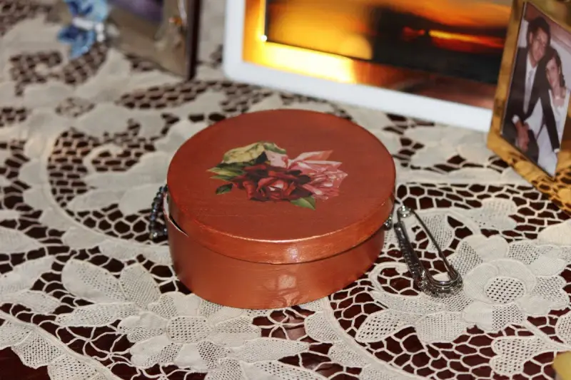 Okrągłe pudełko ozdobione techniką decoupage z motywem róż. Obok broszka i ramka ze zdjęciem.
