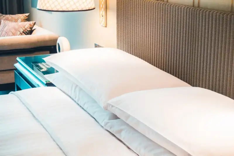 Cama de hotel con almohadas blancas y cabecero de mimbre. Una guía para saber como elegir un colchon.