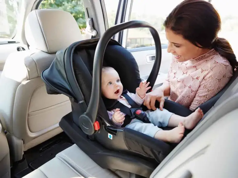 Uśmiechnięta mama patrzy na swojego **noworodka w foteliku samochodowym**, gotowego na podróż.