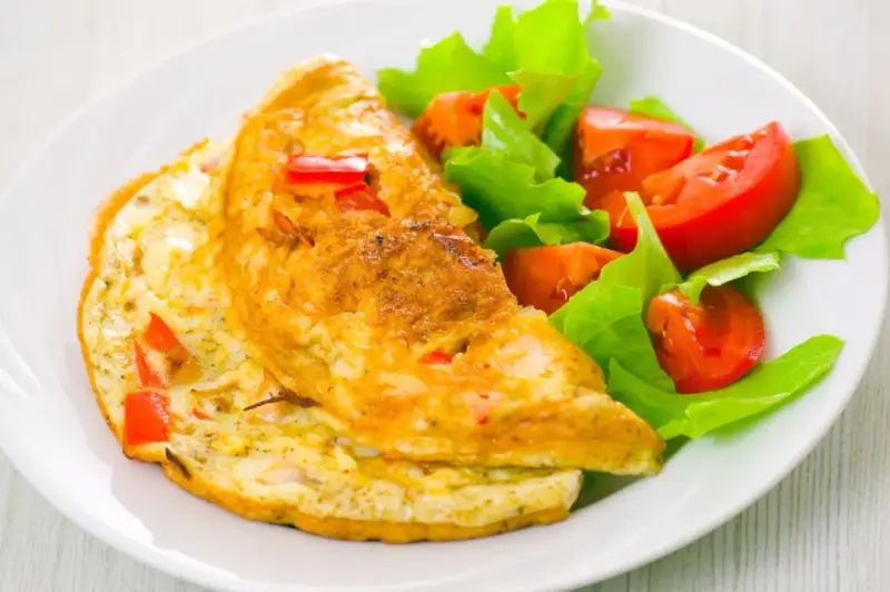 Złocisty omlet francuski z kawałkami papryki, podany z sałatką z pomidorów i sałaty. Pyszne śniadanie.