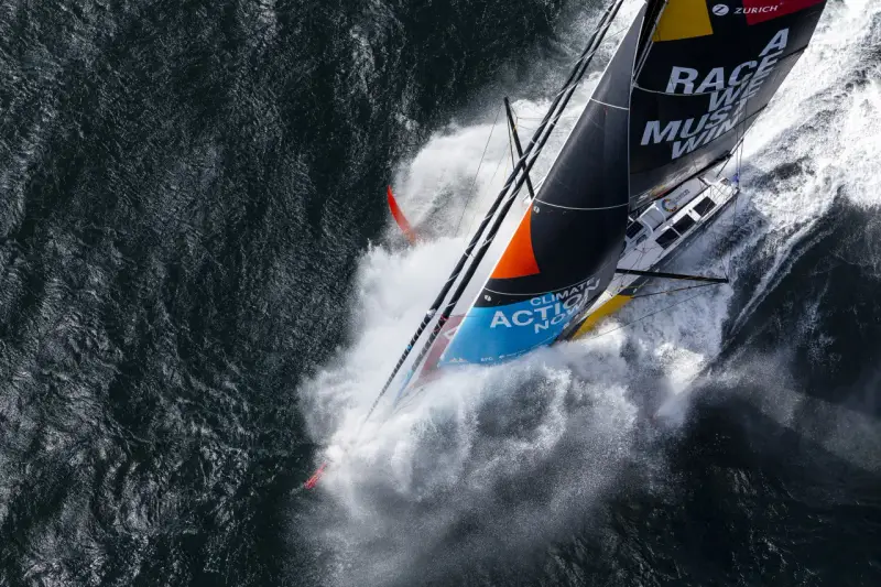 Le voilier de Boris Herrmann fend les vagues, projetant une gerbe d'eau. La voile arbore "Race we must win".