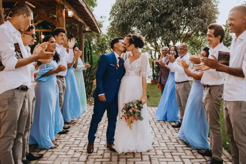 Un couple s'embrasse lors d'un mariage intime, entouré d'invités applaudissant.