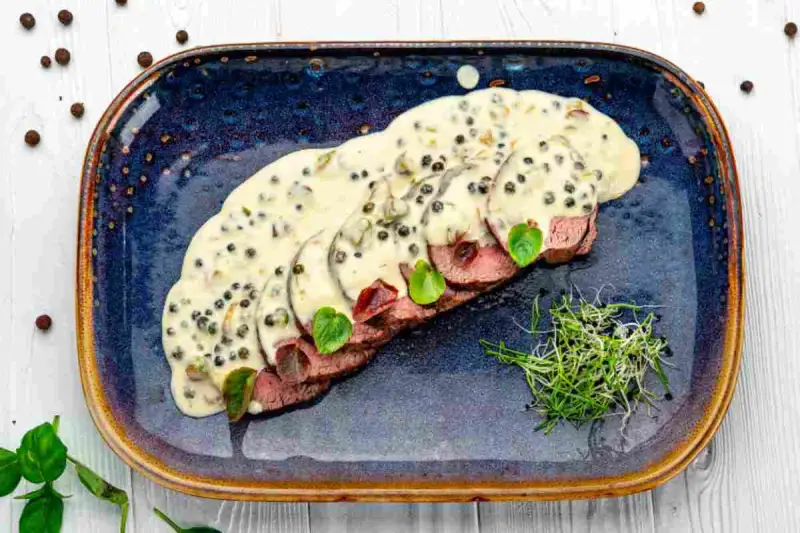 Fette fettine di filetto al pepe verde, ricoperte da una cremosa salsa, guarnite con germogli freschi e foglie verdi.