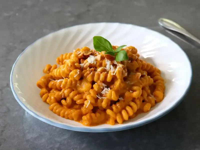 Szybki obiad z makaronem fusilli w kremowym sosie pomidorowym, posypany parmezanem i orzechami, udekorowany listkiem bazylii.