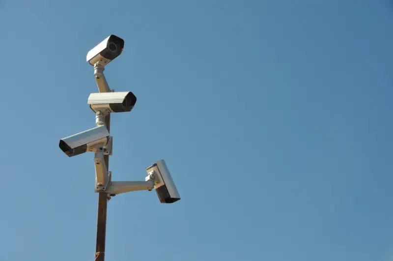 Cztery kamery monitoringu na słupie, czujne oko inwigilacji wpatrujące się w błękitne niebo.