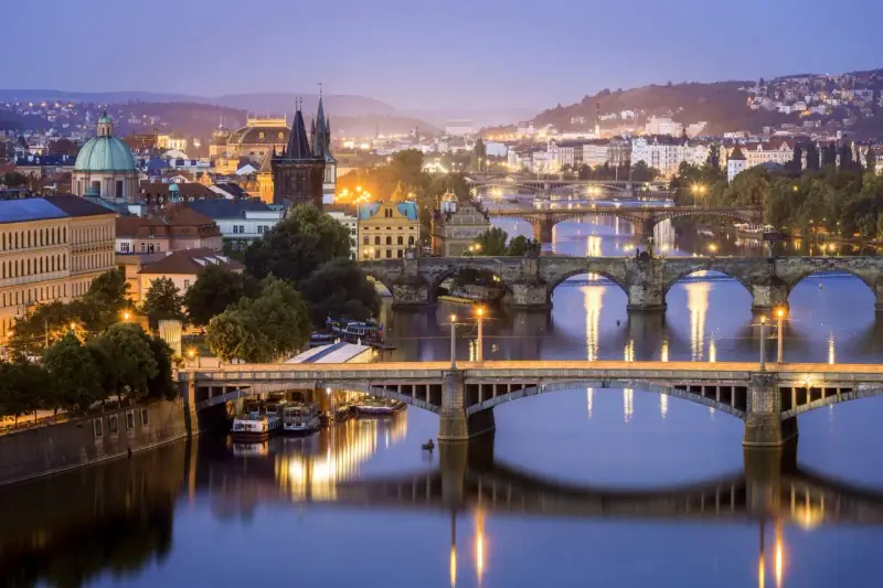 Praga nocą, z licznymi mostami na Wełtawie i oświetlonymi budynkami. Ciekawe ciekawostki o Czechach czekają na odkrycie w tym magicznym mieście.