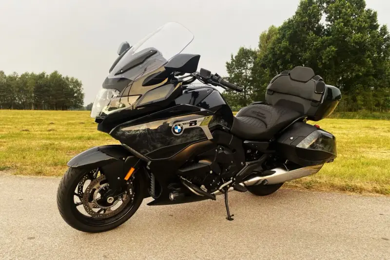Czarny motocykl BMW K1600 Grand America z kuframi, gotowy na daleką podróż pośród zielonych pól i drzew.