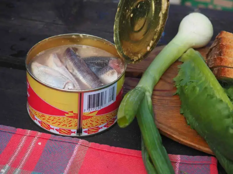 En burk med sill, en klassisk del av **comida tipica sueca**, ligger bredvid färska grönsaker och bröd.